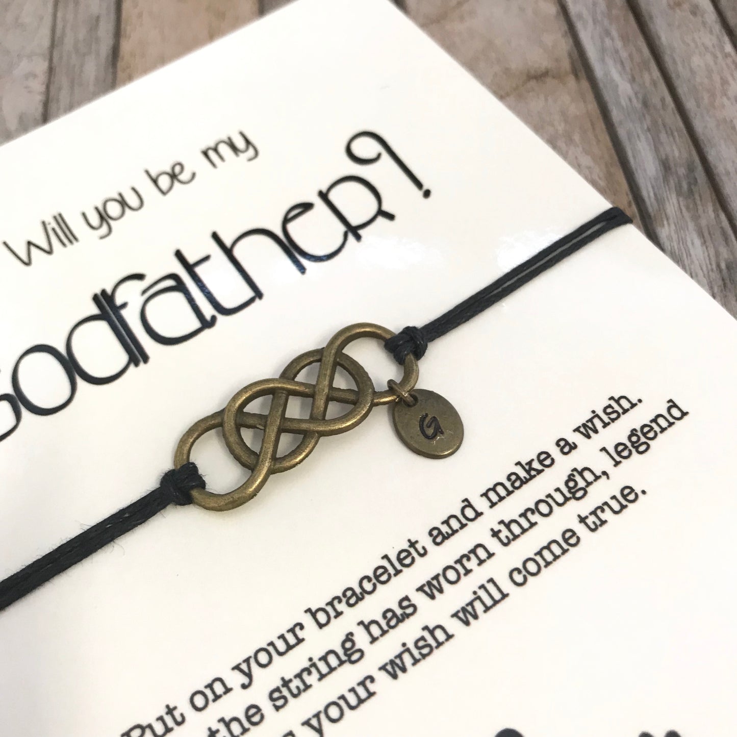 Godfather bracelet with customized initial charm, placed on "Will you be my godfather" proposal card